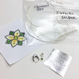 May include: A set of jewelry making supplies including cloisonné wire, eutectic solder, a silver jump ring, a green gemstone, and a sheet of silver foil.
