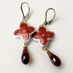 May include: A pair of silver earrings with red enamel flower charms and dangling red faceted teardrop crystals.