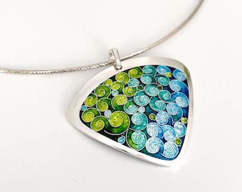 Pode incluir: Um colar de prata com um pingente triangular com um design de esmalte azul e verde em espiral.