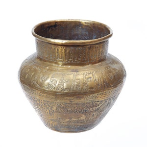 May include: A gold-colored metal vase with intricate engraved designs. The vase has a round body and a wide mouth.