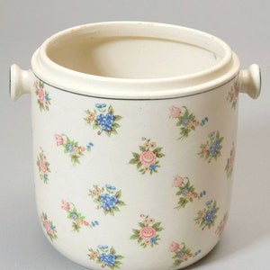 May include: A white ceramic ice bucket with two handles and a floral pattern in shades of pink, blue, and green.