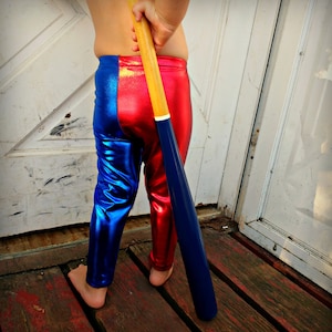 Könnte beinhalten: Ein Kind trägt eine rote und blaue glänzende Leggings und hält einen Holz- und blauen Baseballschläger.