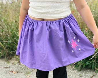 May include: A purple skirt with a pink and white star design. The skirt is gathered at the waist and has a simple, casual style.