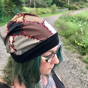 May include: A brown and black beanie with a patchwork design and red stitching. The beanie has a black band around the bottom.