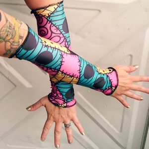 May include: A pair of arm warmers with a colourful patchwork design featuring blue, pink, yellow, and black. The design resembles a popular fictional character.