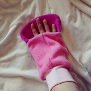 May include: Pink fleece mitten with a pink cuff and a seam down the center. The mitten is designed to fit over the hand and wrist.
