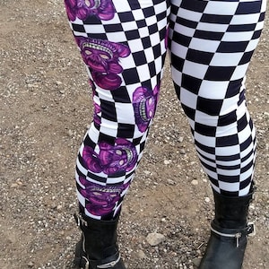 Könnte beinhalten: Schwarz-weiße Karoleggings mit einem lila-weißen Grafikdruck eines grinsenden Gesichts. Die Leggings werden mit schwarzen Stiefeln getragen.