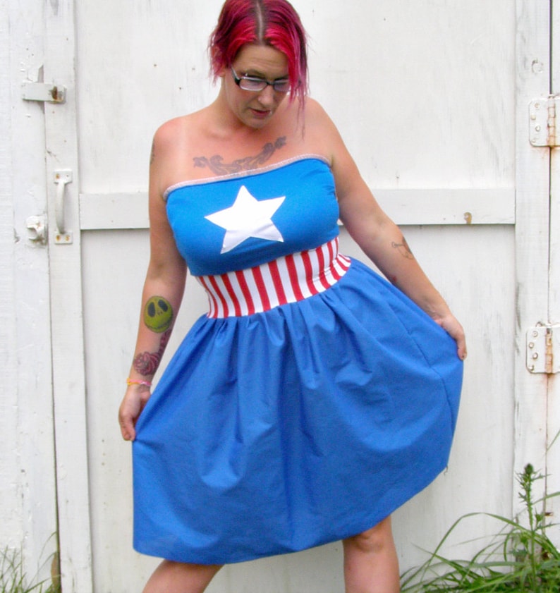 May include: A blue strapless dress with a red and white striped band around the waist and a white star on the bodice. The dress is made of a soft, flowing fabric.