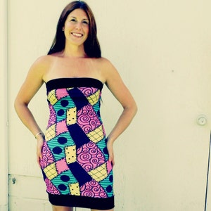 May include: A strapless dress with a patchwork design featuring pink, yellow, blue, and black fabric. The dress has a fitted silhouette and a black waistband.