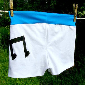 Pode incluir: Shorts brancos com uma cintura azul e um gráfico de nota musical preta.