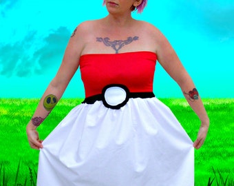 May include: A woman wearing a red and white Poké Ball dress. The dress has a black belt with a white circle in the center. The woman has red hair and is wearing glasses.