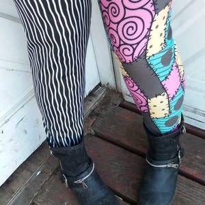 May include: Leggings with two different patterns. One leg features black and white vertical wavy stripes. The other leg has a patchwork design with pink swirls, gray patches, and blue and yellow squares. Both legs are paired with black ankle boots.