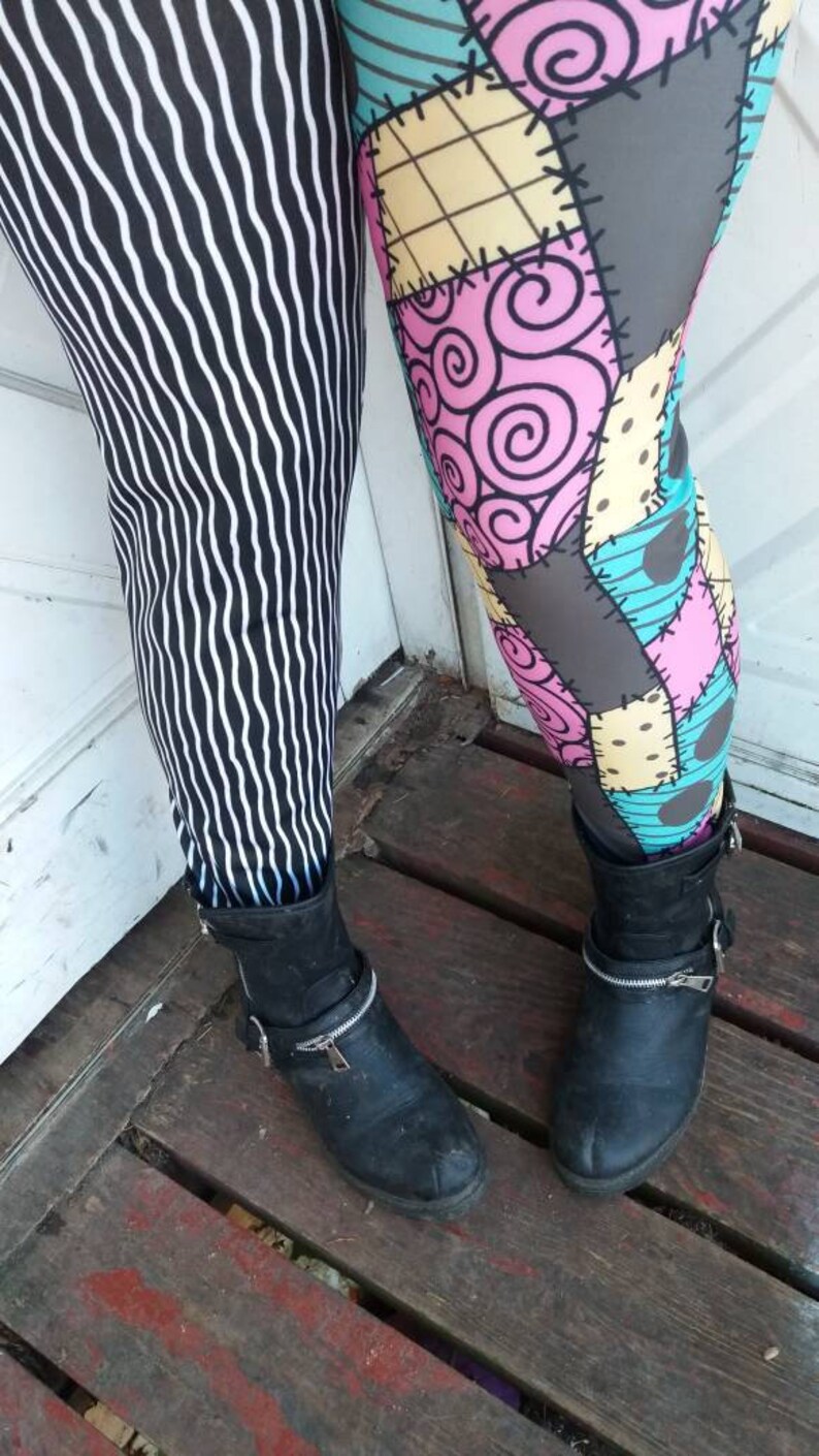 May include: Leggings with two different patterns. One leg features black and white vertical wavy stripes. The other leg has a patchwork design with pink swirls, gray patches, and blue and yellow squares. Both legs are paired with black ankle boots.