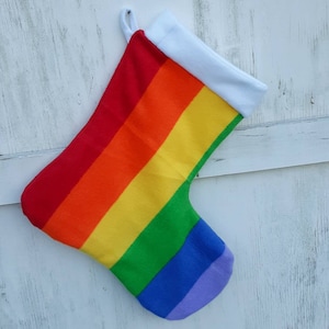 May include: A rainbow-striped Christmas stocking with a white cuff and hanging loop. The stocking features the colors of the rainbow: red, orange, yellow, green, blue, and purple. The stocking is made of a soft fabric.