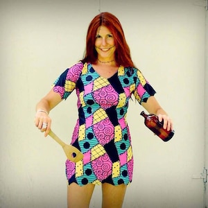 May include: A woman dressed as Sally from The Nightmare Before Christmas. She is wearing a patchwork dress with black, pink, yellow and blue fabric. She is holding a wooden spoon and a bottle.