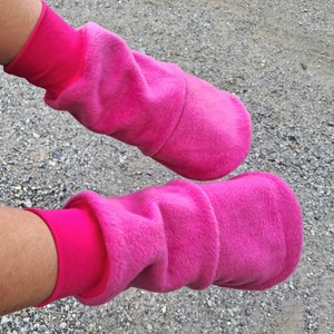 May include: A pair of pink fleece leg warmers with a fold-over cuff. The leg warmers are made of a soft, fuzzy material and are perfect for keeping your legs warm in the winter.