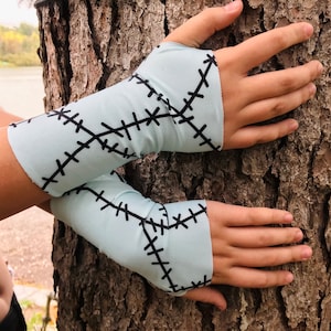 May include: A pair of light blue arm warmers with black stitching in a criss-cross pattern. The arm warmers are made of a soft, stretchy fabric.