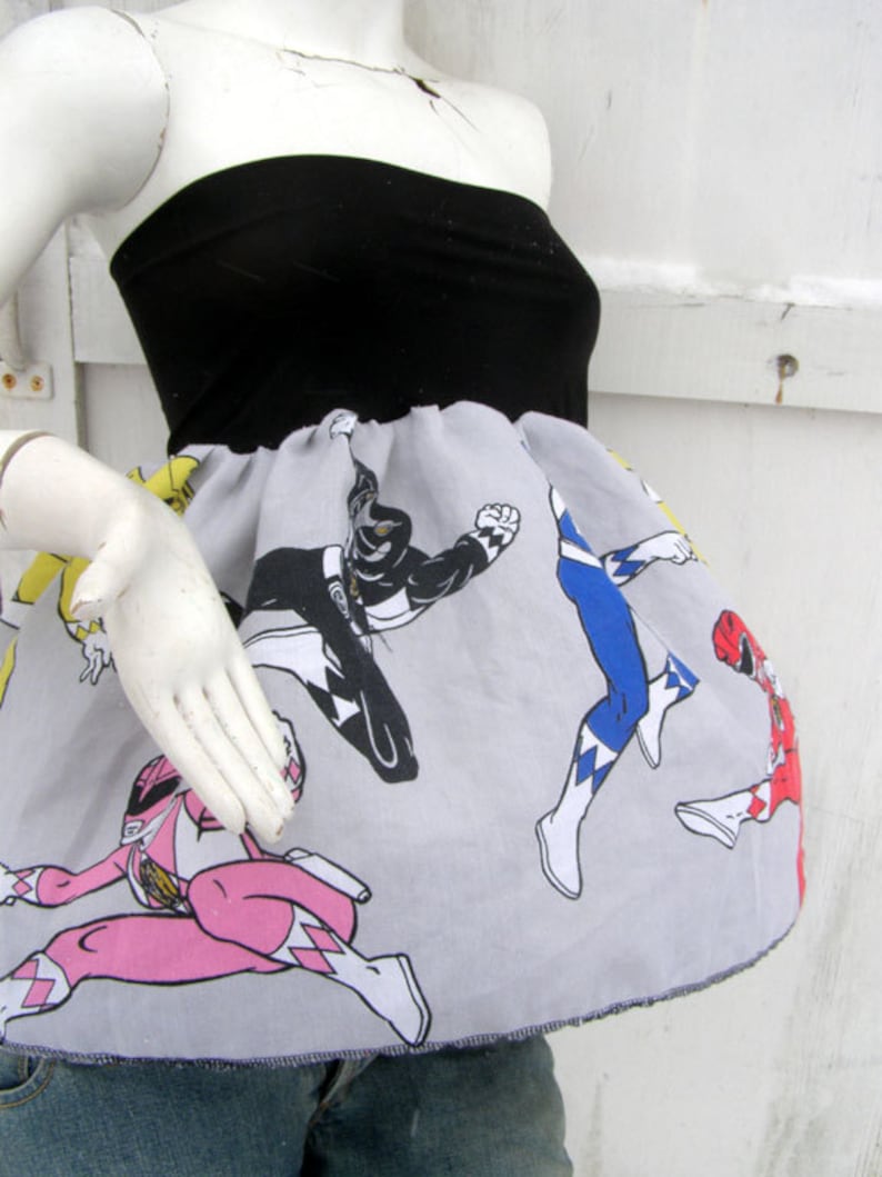 K&ouml;nnte beinhalten: Ein graues und wei&szlig;es tr&auml;gerloses Kleid mit einem schwarzen Oberteil und einem Aufdruck der Power Rangers. Der Aufdruck zeigt die Red, Blue, Black und Pink Rangers.