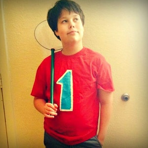 May include: A person wearing a red t-shirt with a large blue number one on the front. They are holding a green net on a stick.