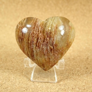 May include: A heart-shaped polished stone with brown and white stripes. The stone is on a clear plastic stand.