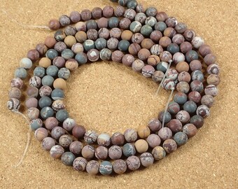 May include: A strand of round, multi-colored, patterned beads. The beads are a mix of brown, gray, and white. The beads are strung on a clear thread.