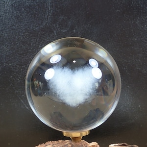 May include: A clear glass sphere with a white cloud-like shape inside. The sphere is sitting on a dark surface.