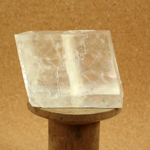 Puede incluir: Un cristal transparente y translúcido con forma rectangular. El cristal está sentado sobre un soporte de madera.