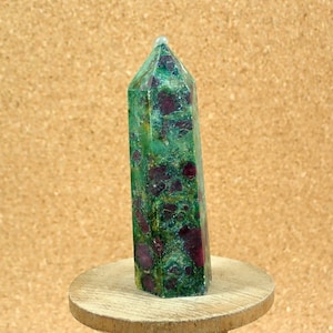 May include: A green and red gemstone point, also known as a crystal, with a pointed top and a flat base. The gemstone is a natural, unpolished, and rough-cut crystal.