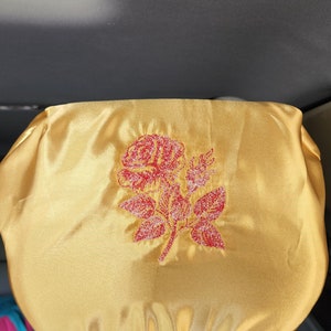 May include: A gold car seat headrest cover with a red embroidered rose design.