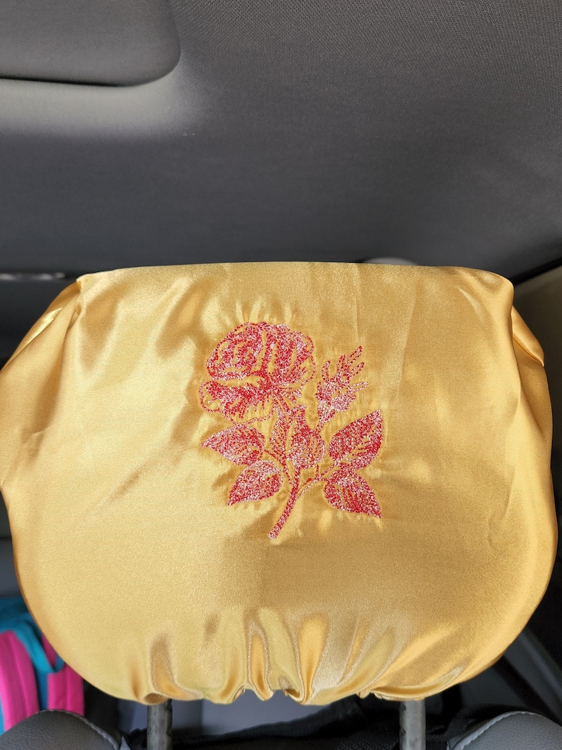 May include: A gold car seat headrest cover with a red embroidered rose design.