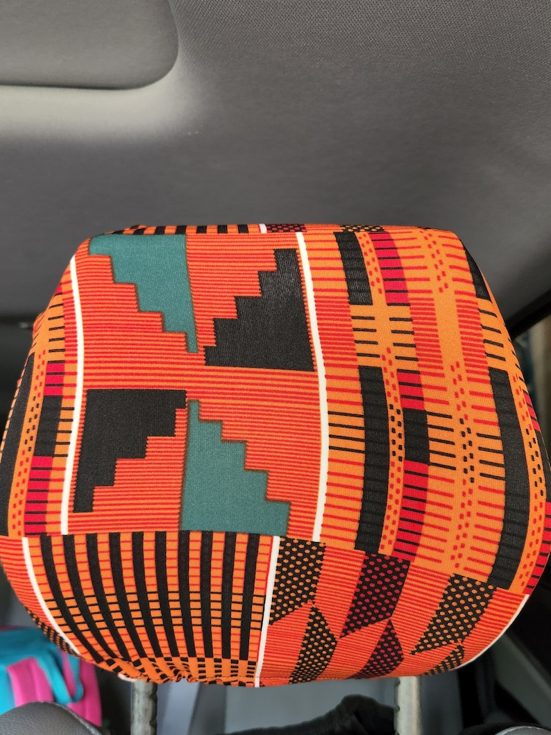 May include: A colorful headrest cover with a geometric pattern in shades of orange, black, white, red, and teal. The pattern is reminiscent of African Kente cloth.
