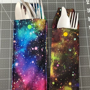 May include: Two zippered pouches with a galaxy print. One pouch contains a fork, spoon, and straw. The other pouch contains a fork and spoon. Both pouches have a yellow button.