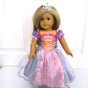 May include: A doll wearing a princess dress with a silver tiara. The dress has a pink bodice with yellow lacing and a pink and silver skirt. The doll has blonde hair and is standing in front of a white background.