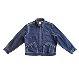 May include: A dark blue denim jacket featuring a full-length front zipper, a pointed collar, and long sleeves. The garment includes a single slanted chest pocket with a zipper closure and two lower front pockets, all accented with white stitching.