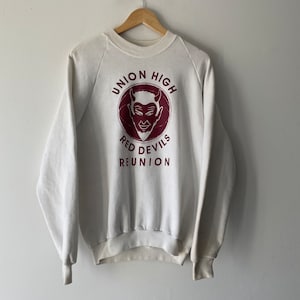 Puede incluir: Sudadera blanca con un gráfico granate de una cabeza de diablo en un círculo con el texto "Union High Red Devils Reunion".