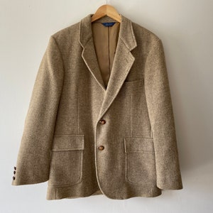 Puede incluir: Una chaqueta de tweed marrón con dos botones de cierre y dos bolsillos de solapa. La chaqueta tiene un corte clásico y un sutil patrón de espiga.
