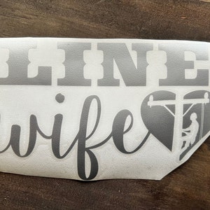 May include: A gray vinyl decal with the text "LINE wife" and a heart-shaped silhouette of a lineman working on a power pole.