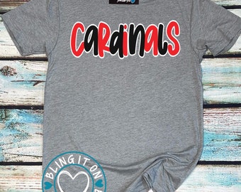 Peut inclure: T-shirt gris avec le mot "Cardinals" en lettres rouges et noires. Le t-shirt est sur un fond en bois avec un logo en forme de cœur qui dit "Bling It On".