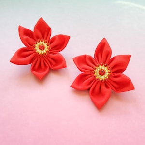Puede incluir: Dos pinzas para el pelo de flores rojas de tela con centros dorados y diamantes de imitación rojos.