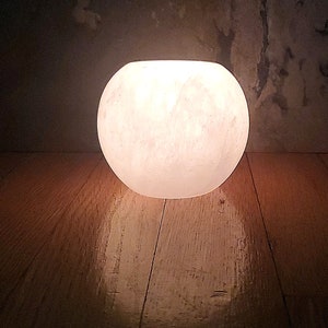 May include: A white, round, salt lamp with a warm glow. The lamp is sitting on a wooden surface.