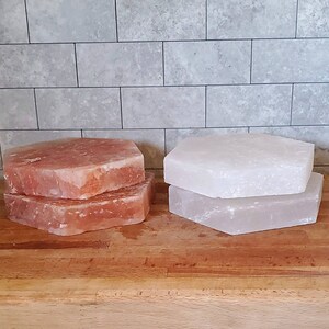 May include: Two sets of Himalayan salt slabs, one set is pink and the other is white. The slabs are stacked on top of each other and are sitting on a wooden surface.