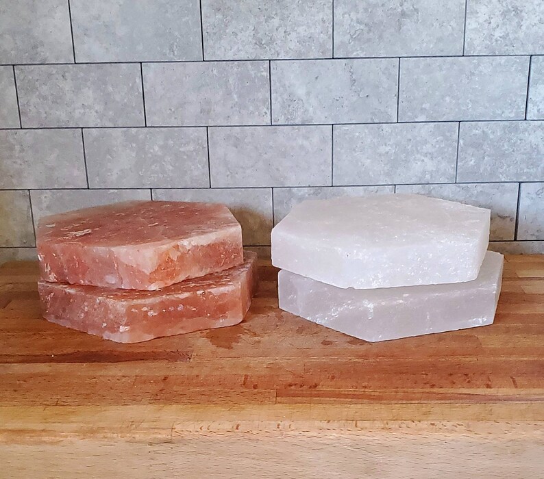May include: Two sets of Himalayan salt slabs, one set is pink and the other is white. The slabs are stacked on top of each other and are sitting on a wooden surface.