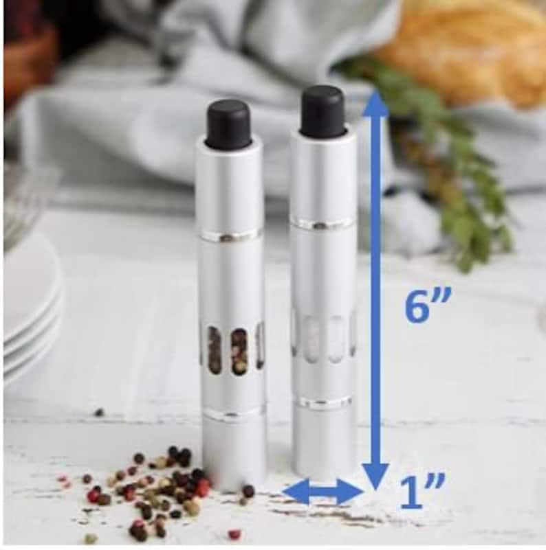May include: Two silver pepper and salt grinders with black tops. The grinders are 6 inches tall and 1 inch in diameter.