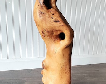May include: A wooden sculpture of a face with a large opening in the side. The sculpture is made of light brown wood with a natural finish.