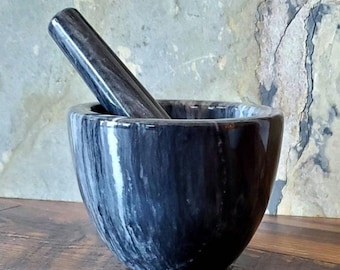 May include: Black and white marble mortar and pestle set. The mortar is a deep bowl with a wide rim and the pestle is a smooth, rounded cylinder.