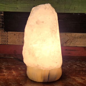 May include: A white Himalayan salt lamp with a wooden base. The lamp is lit and glowing.