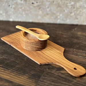 May include: A wooden serving board with a small wooden bowl and spoon. The bowl and spoon are made of the same wood as the board.