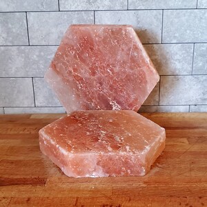 May include: Two hexagonal pink Himalayan salt slabs, one stacked on top of the other. The slabs are rough and have a natural, uneven texture.