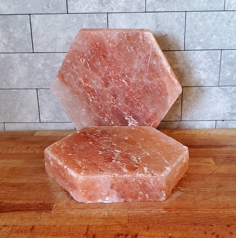 May include: Two hexagonal pink Himalayan salt slabs, one stacked on top of the other. The slabs are rough and have a natural, uneven texture.