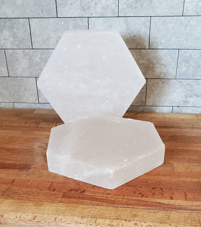 May include: Two white hexagonal Himalayan salt plates, one stacked on top of the other. The plates are smooth and have a slightly rough texture.